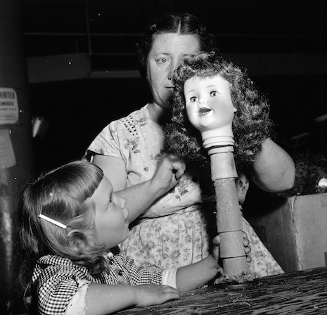 Doll factory working working on a doll head on a stick, 1955