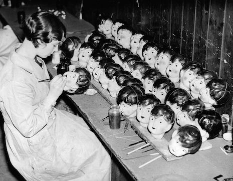 A doll worker in a factory in England painting doll heads, 1935