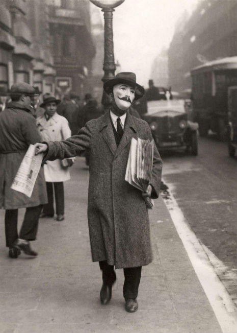 Man selling newspapers in Paris looks like he’s wearing a Guy Fawkes mask, 1925